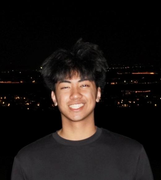 Smiling Ardy in a black shirt with city lights in the background at night.